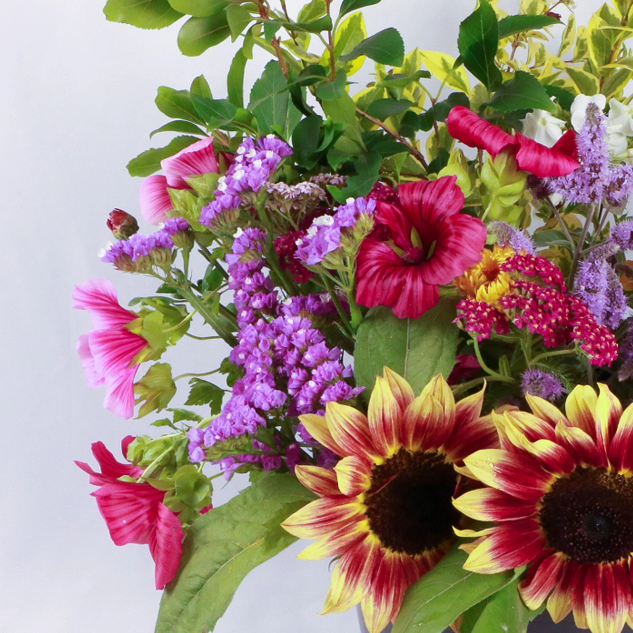 Close-up of Marguerite Rose's DIY flower bucket from the left, highlighting freshly picked Devon grown flowers: red-yellow sunflowers, purple statice, pink cosmos, celosia, and vibrant green foliage.