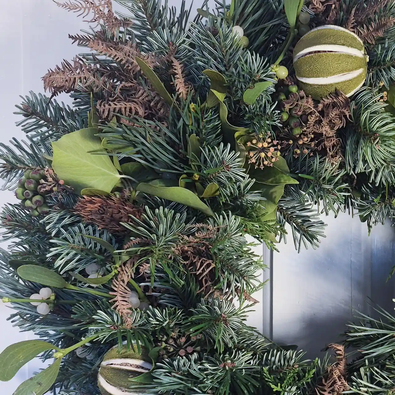 Close-up of handmade Devon Christmas wreath showing foraged mistletoe, dried citrus slices, seed heads and bronzed foliage