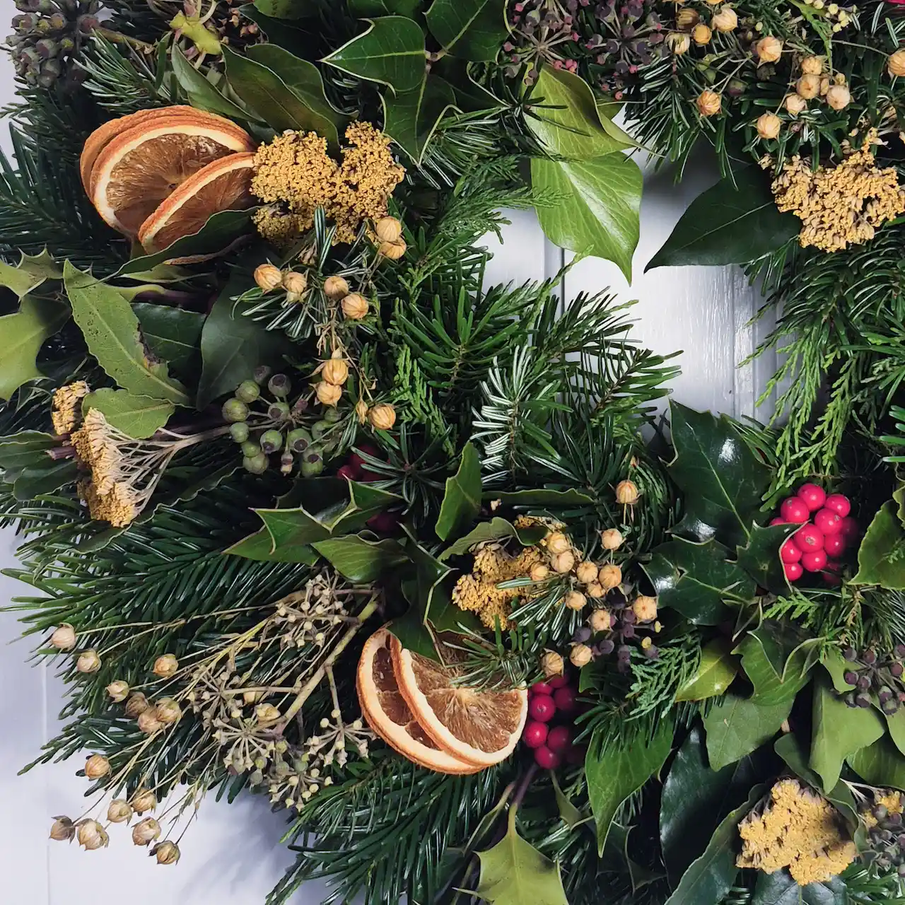 Close-up of handmade Devon Christmas wreath showing dried orange slices, golden achillea, holly berries and pine