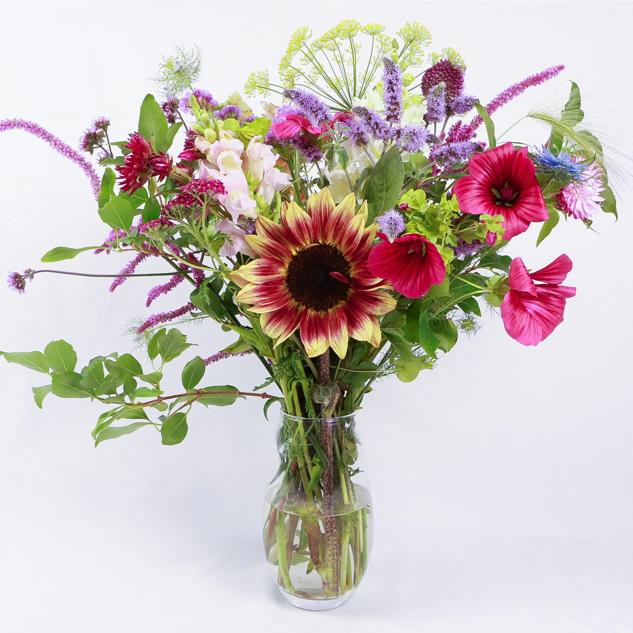 Large seasonal bouquet in glass vase with sunflowers, pink cosmos, purple veronica, dill flowers, and mixed foliage grown in Devon