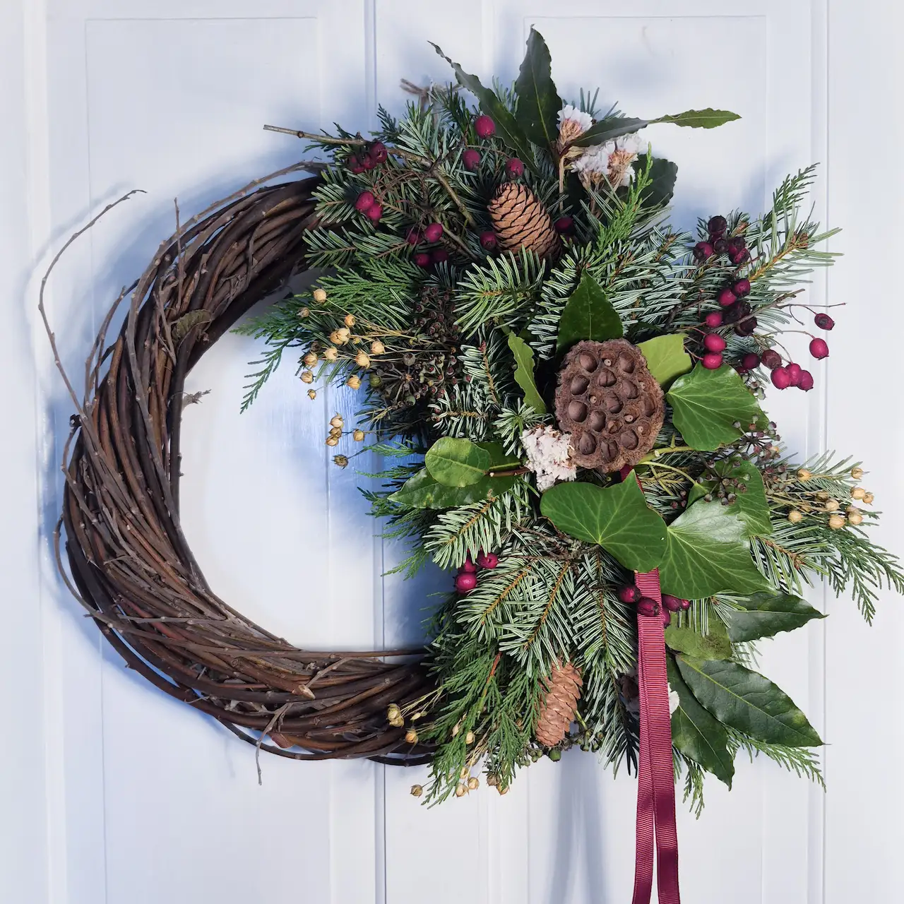 The Winter Berry large willow Christmas wreath with burgundy hawthorn berries, lotus pods, ivy, pine cones and pine handmade in Devon with handwoven willow base