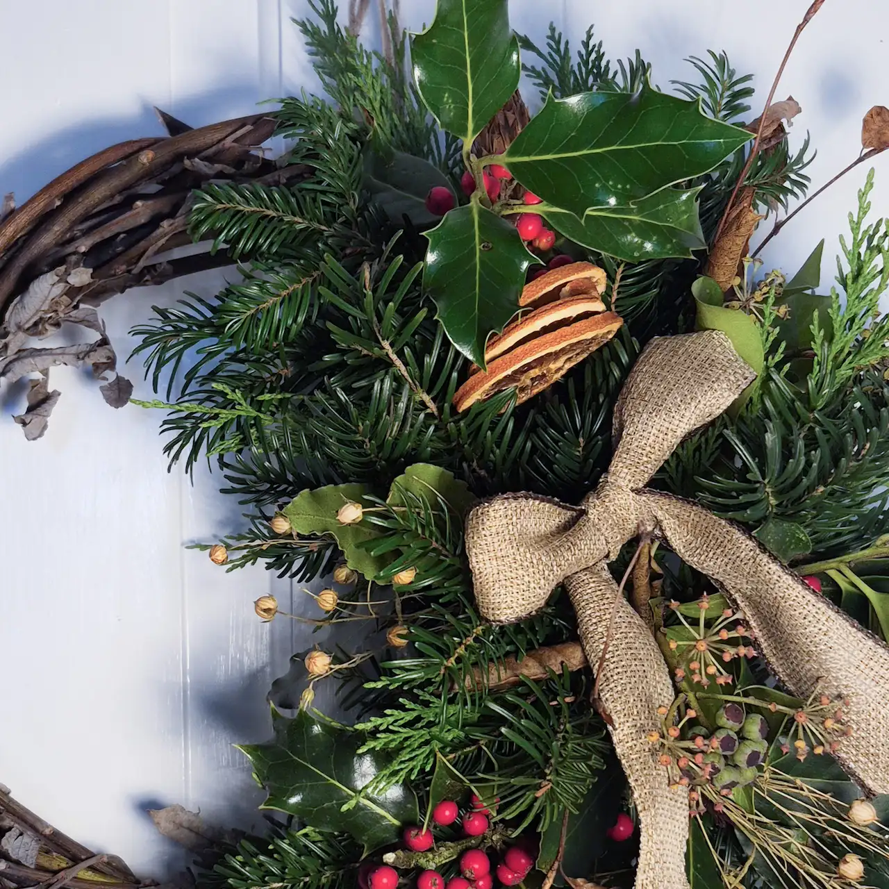Close-up of Devon willow Christmas wreath featuring glossy holly with berries, dried orange slices, bay leaves and pine
