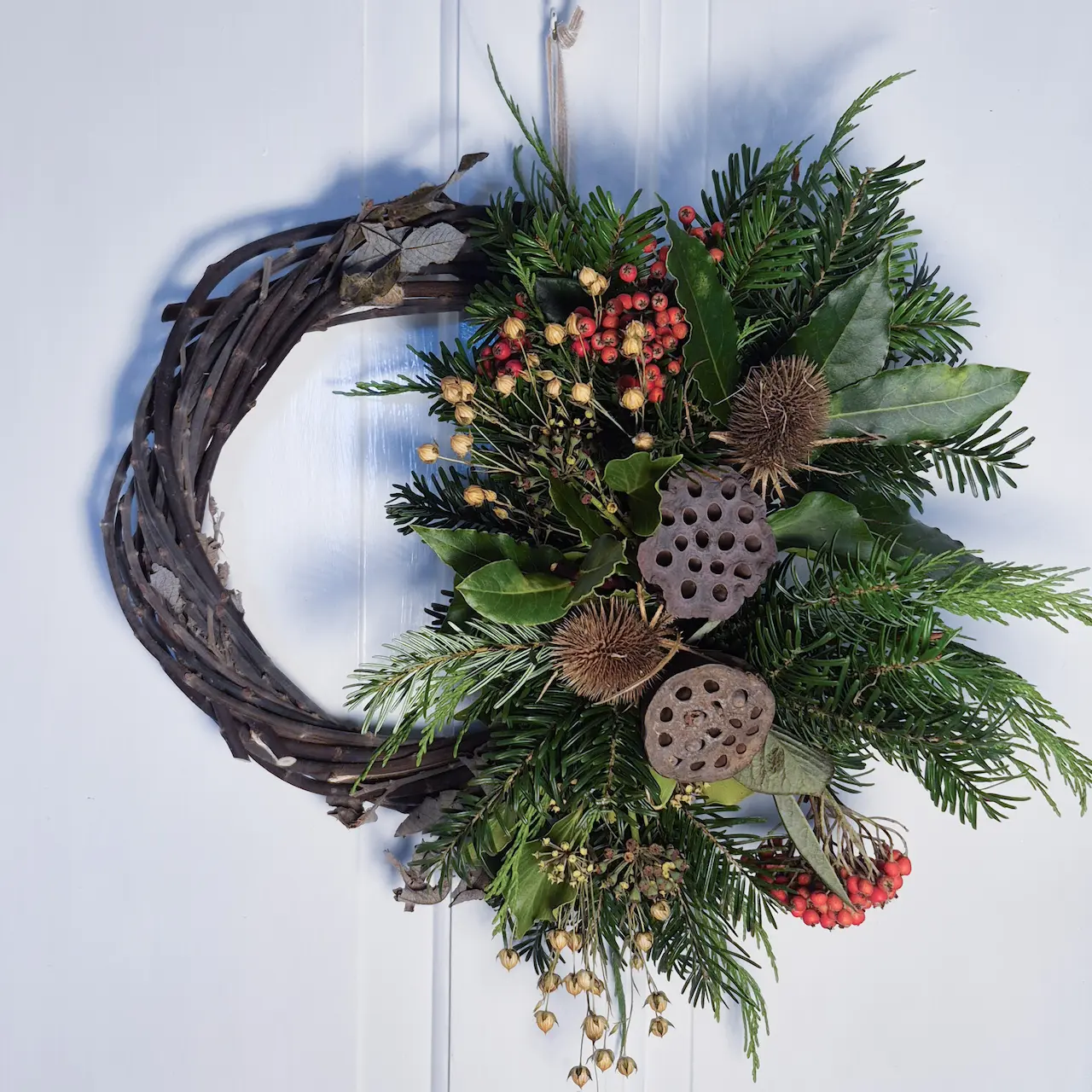 The Wild Garden small willow Christmas wreath with red cotoneaster berries, lotus pods, teasels, bubble grass, pine, bay and ivy handmade in Devon with handwoven willow base